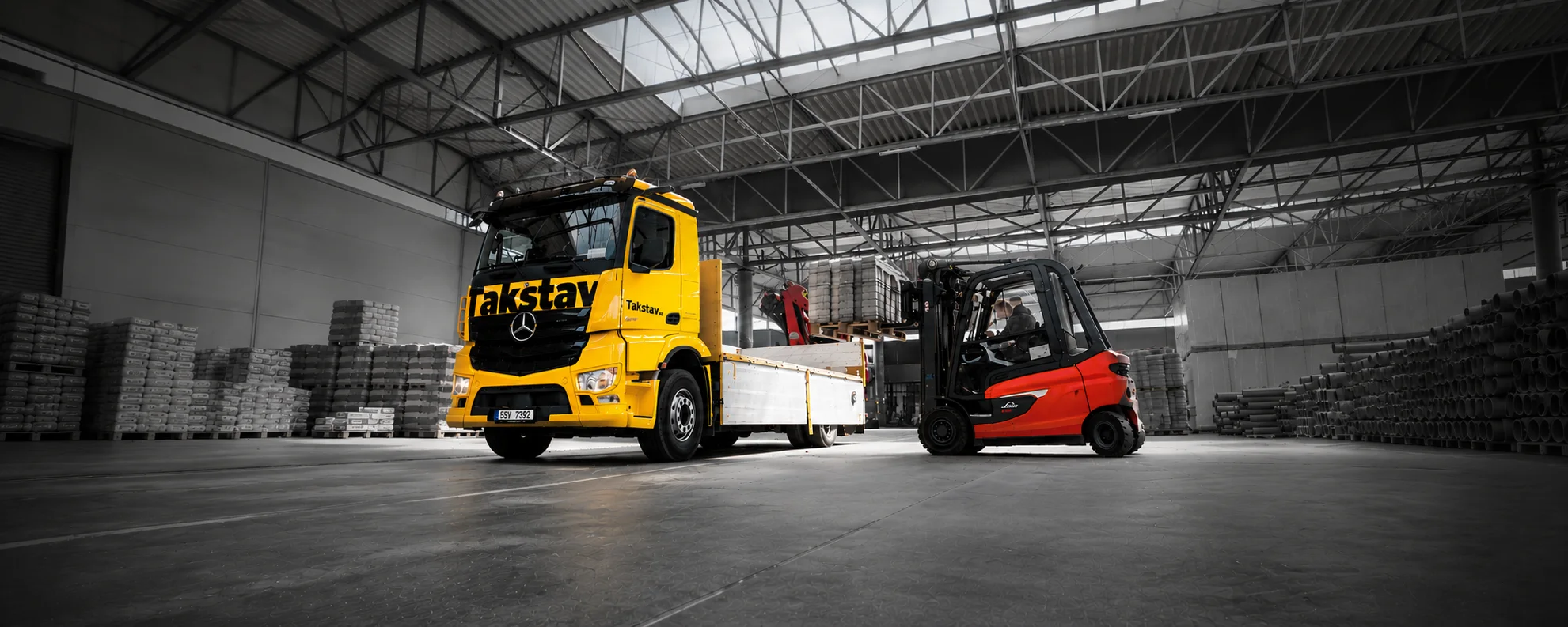 Žlutý nákladní vůz Takstav při nakládce stavebního materiálu ve skladu